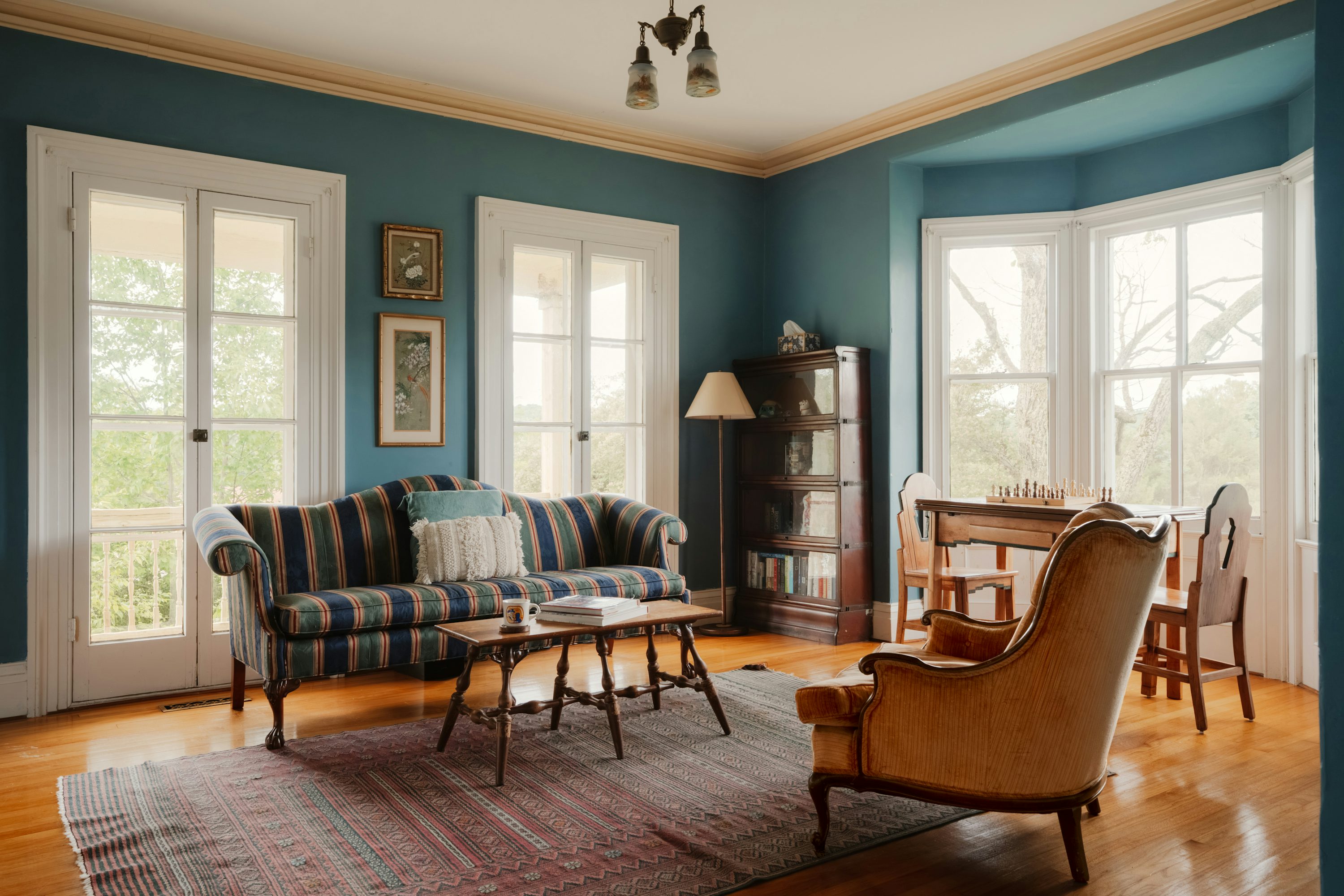 Soggiorno in stile classico con divano a righe, poltrona imbottita e scrivania in legno: atmosfera elegante e arredi tradizionali.
