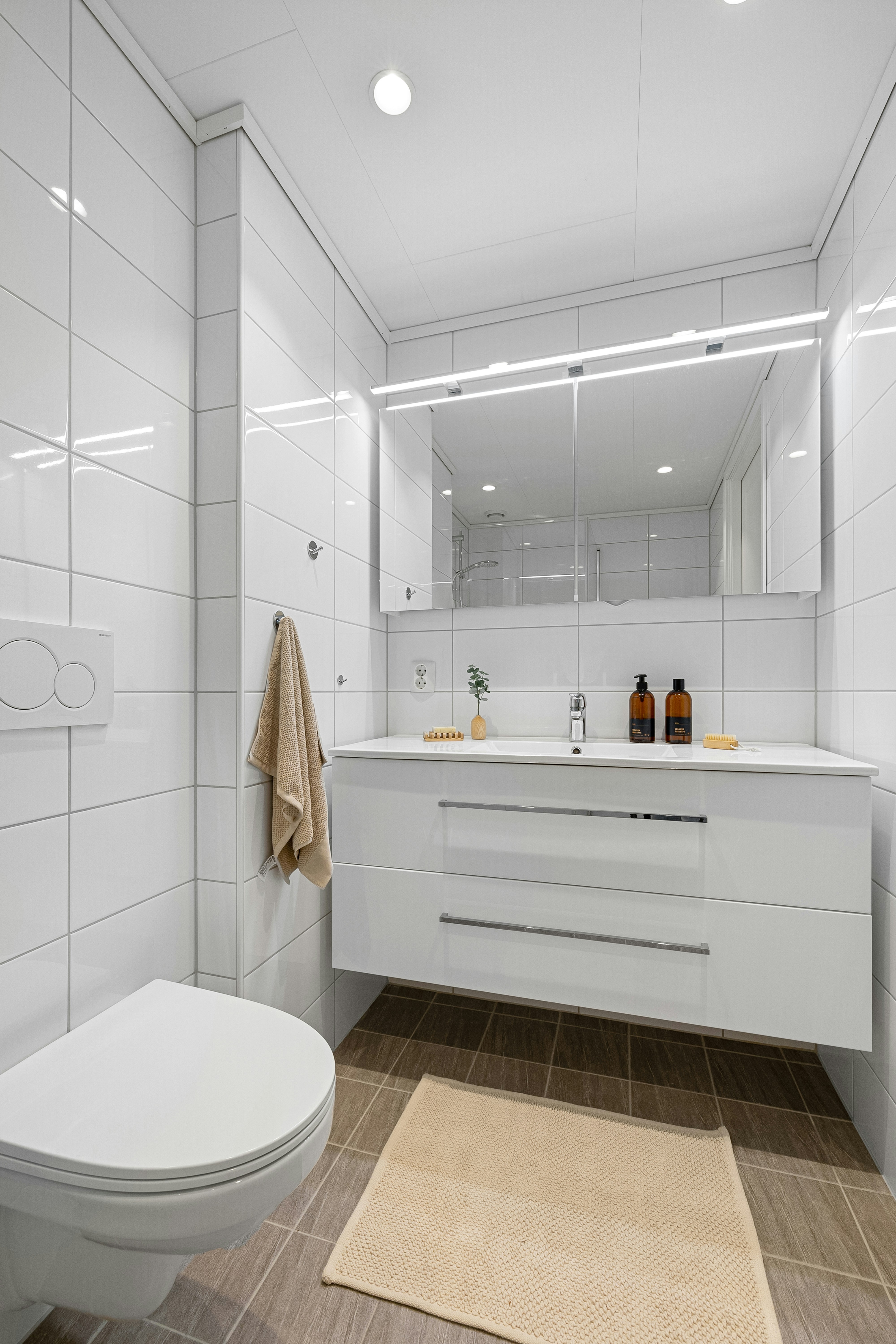Bagno moderno con mobile sospeso, lavabo e specchiera luminosa, WC a denuncia bianca e tappeto beige sul pavimento in