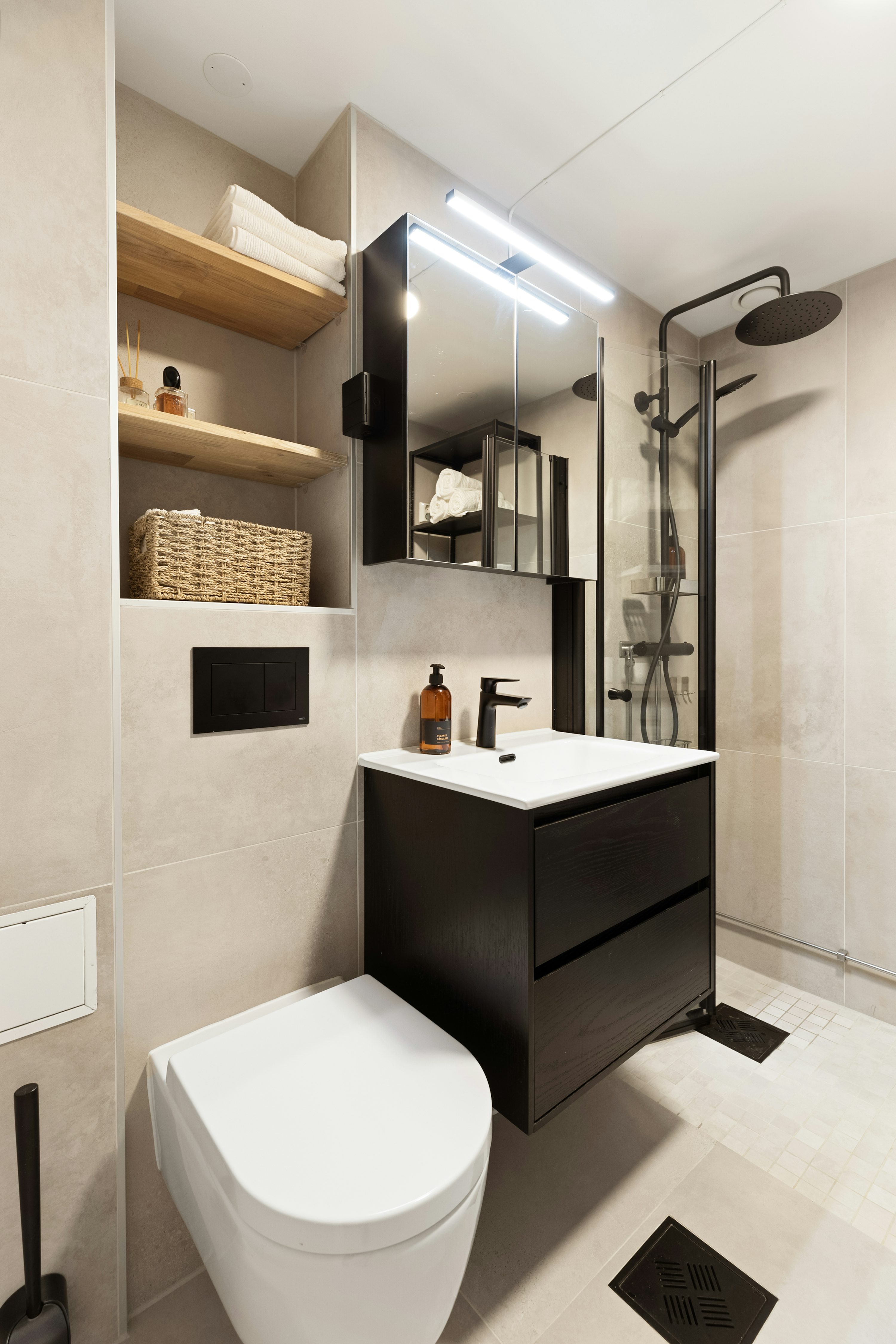 Bagno moderno con lavabo nero a muro e mobiletto, toilette bianca, mensole a sinistra e doccia con soffione nero.