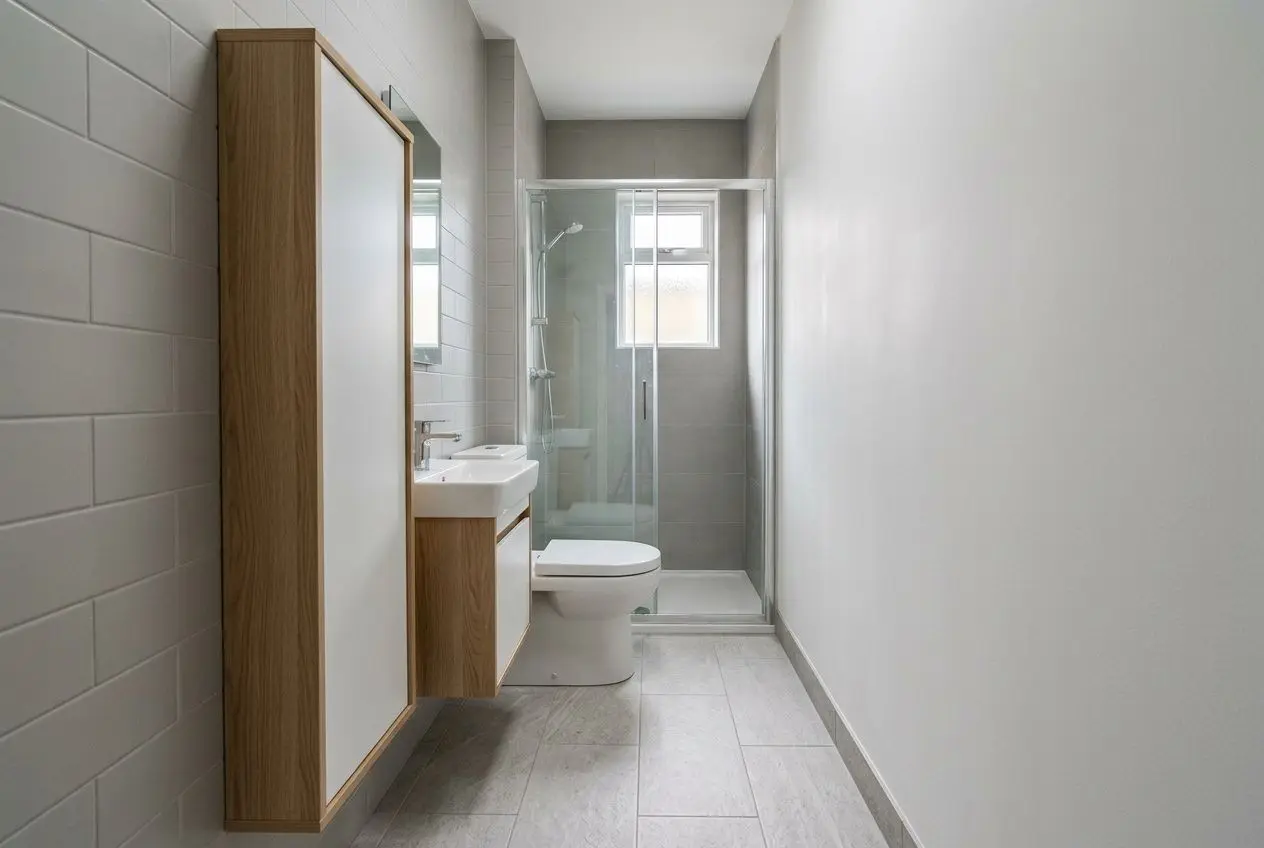 Bagno piccolo rettangolare moderno con lavabo su mobile, wc e doccia incorniciata in vetro, illuminato da finestra.