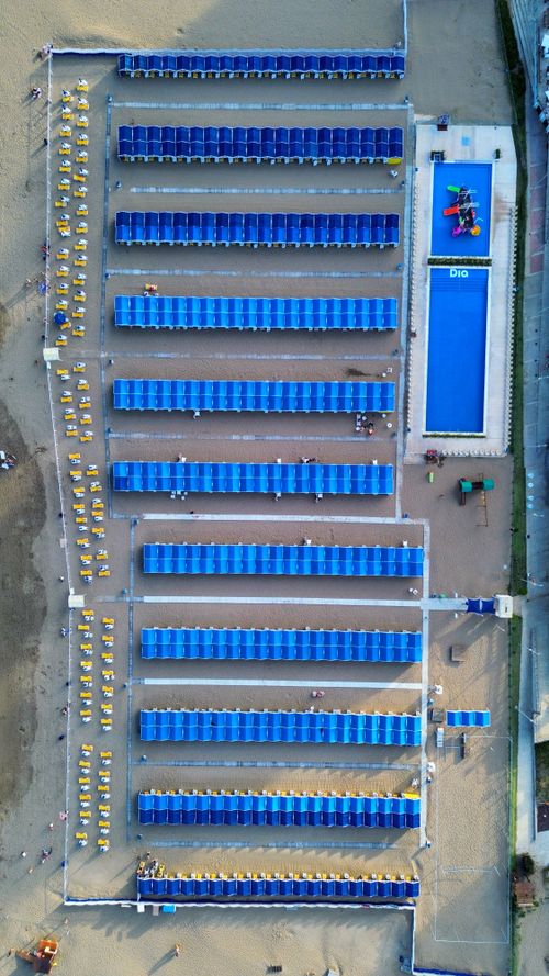 Vista dall'alto di una piscina sul mare con file ordinate di lettini blu e sedie gialle.