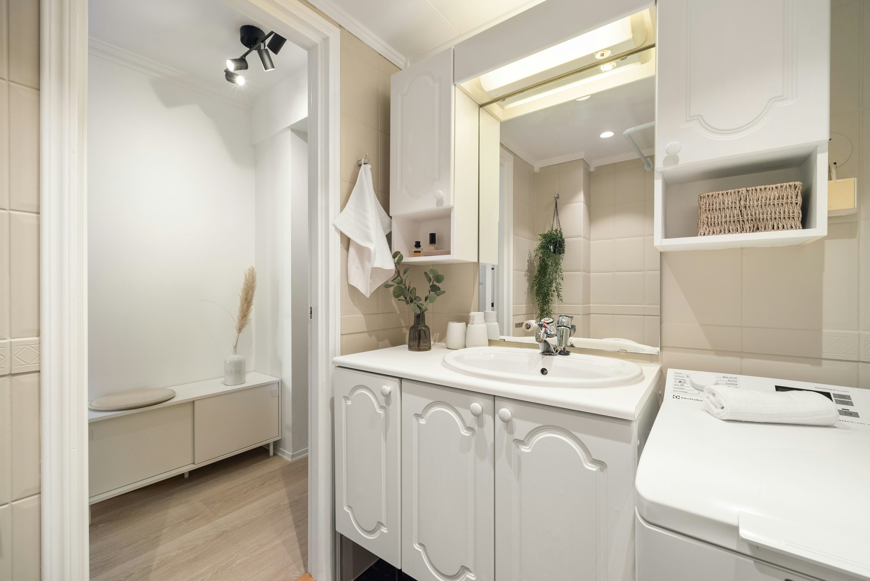 Bagno moderno con lavabo bianco, mobiletti a anta dettagliata e grande specchio illuminato, con asciugamani appesi e piante